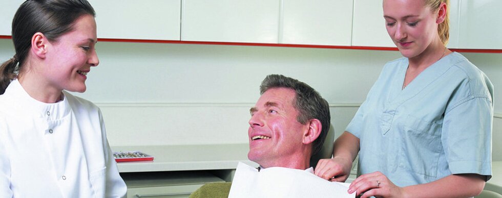 A man being prepared for dental examination by two nurses